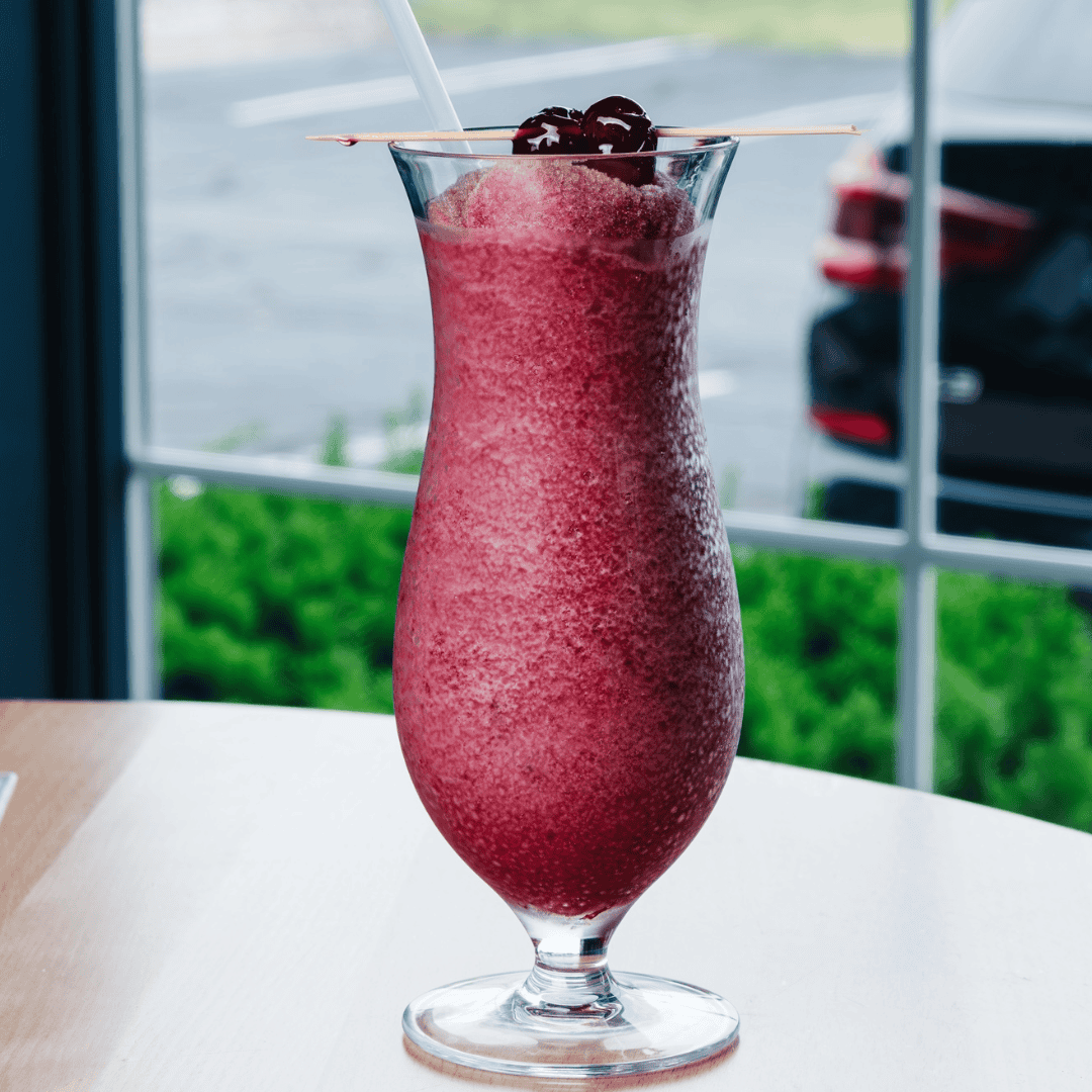 Purple color beer slushy with cherries on top on a table in front of a window